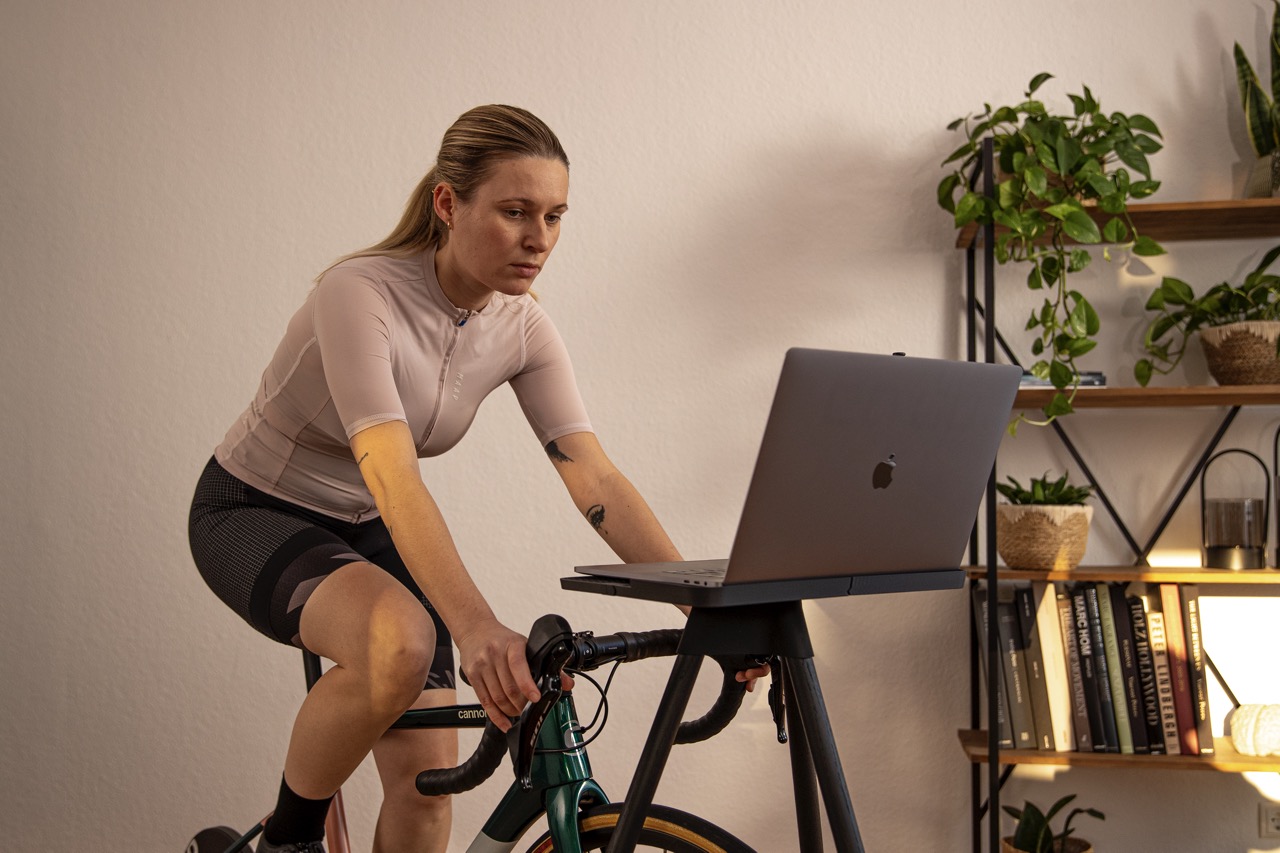 Woman sitting on indoor cycling bike. In front of her is a laptop.
