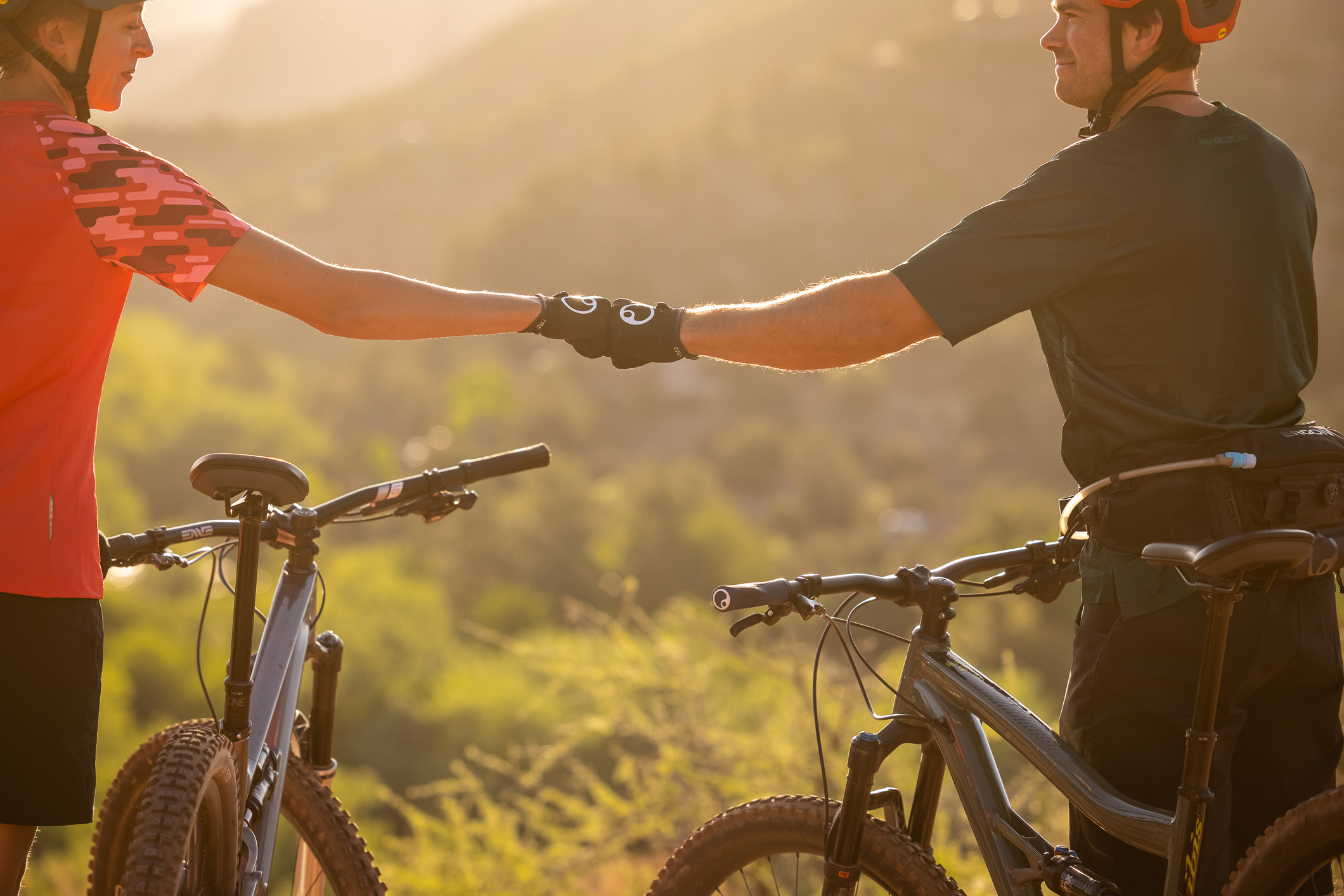 Two mountain bikers fist bump in the desert wearing Ergon HM2 gloves. 