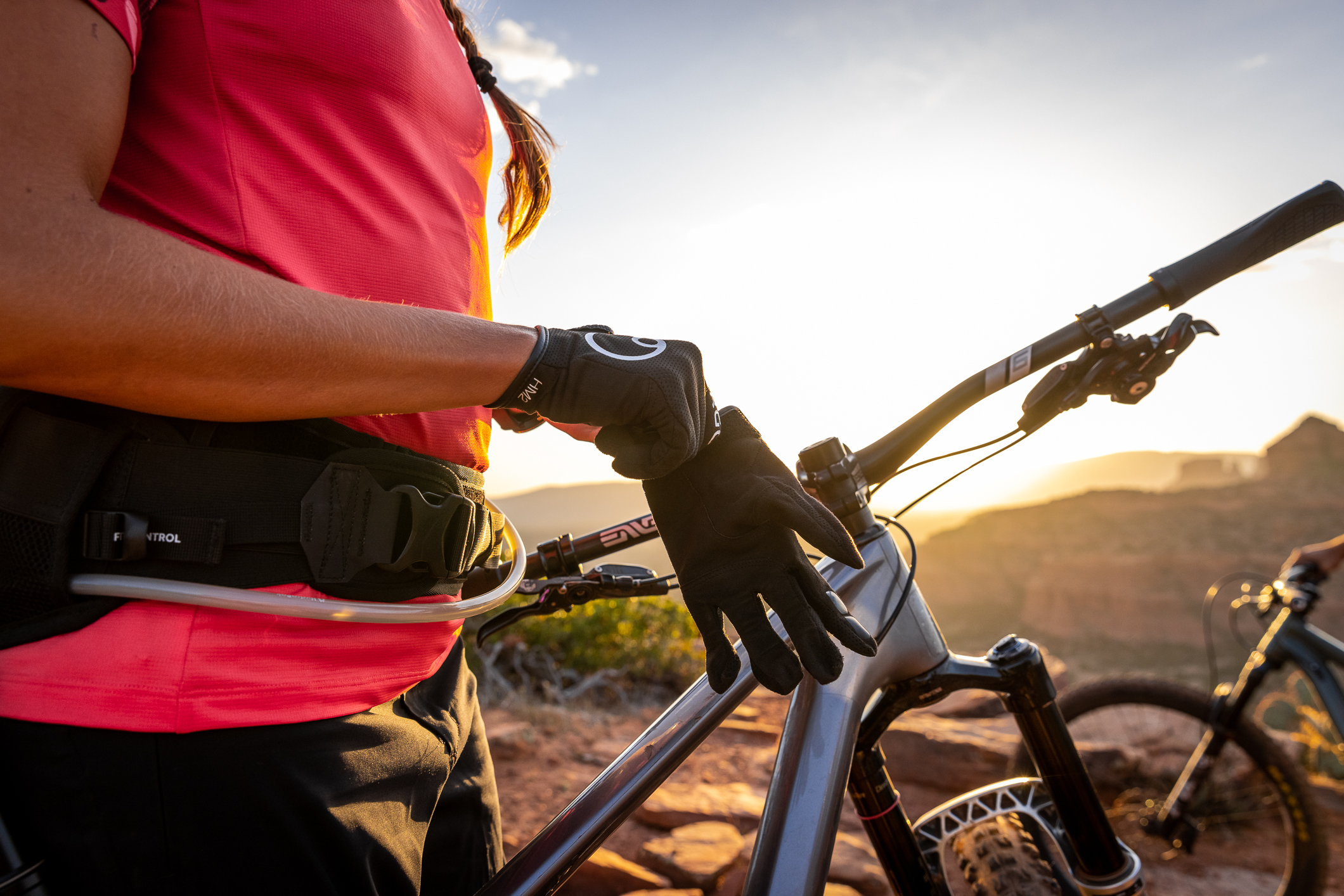 Ergon Mountainbikerin zieht ihre HM2 Handschuhe an, Sonnenuntergang im Hintergrund. 