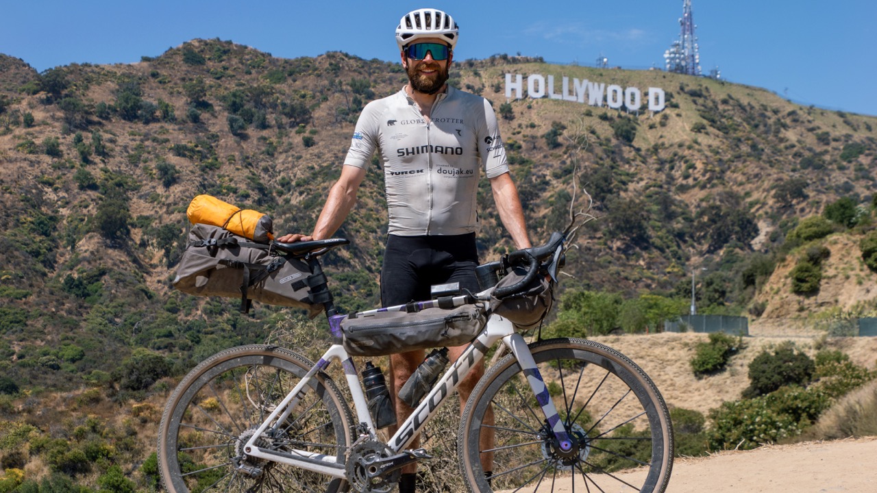 Jonas Deichmann steht mit seinem vollbepackten Gravelbike vor dem berühmten Hollywood-Schild. Mit Ergon-Ausrüstung ausgestattet, verkörpert er Abenteuerlust und Ausdauer.