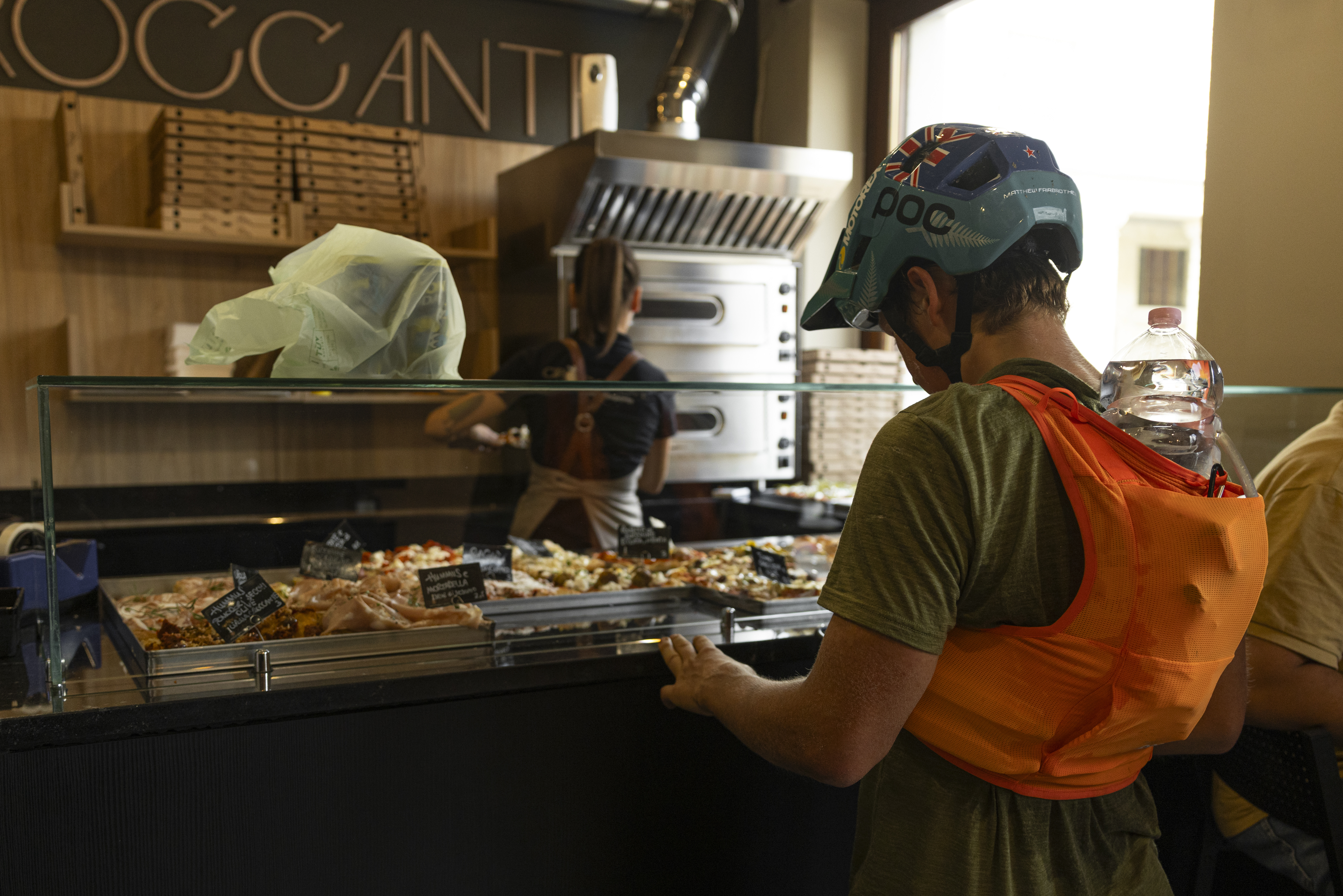 Matthew Fairbrother stands in a bakery/pizzeria, surrounded by food displays, refueling during his ride with Ergon saddle and grips.