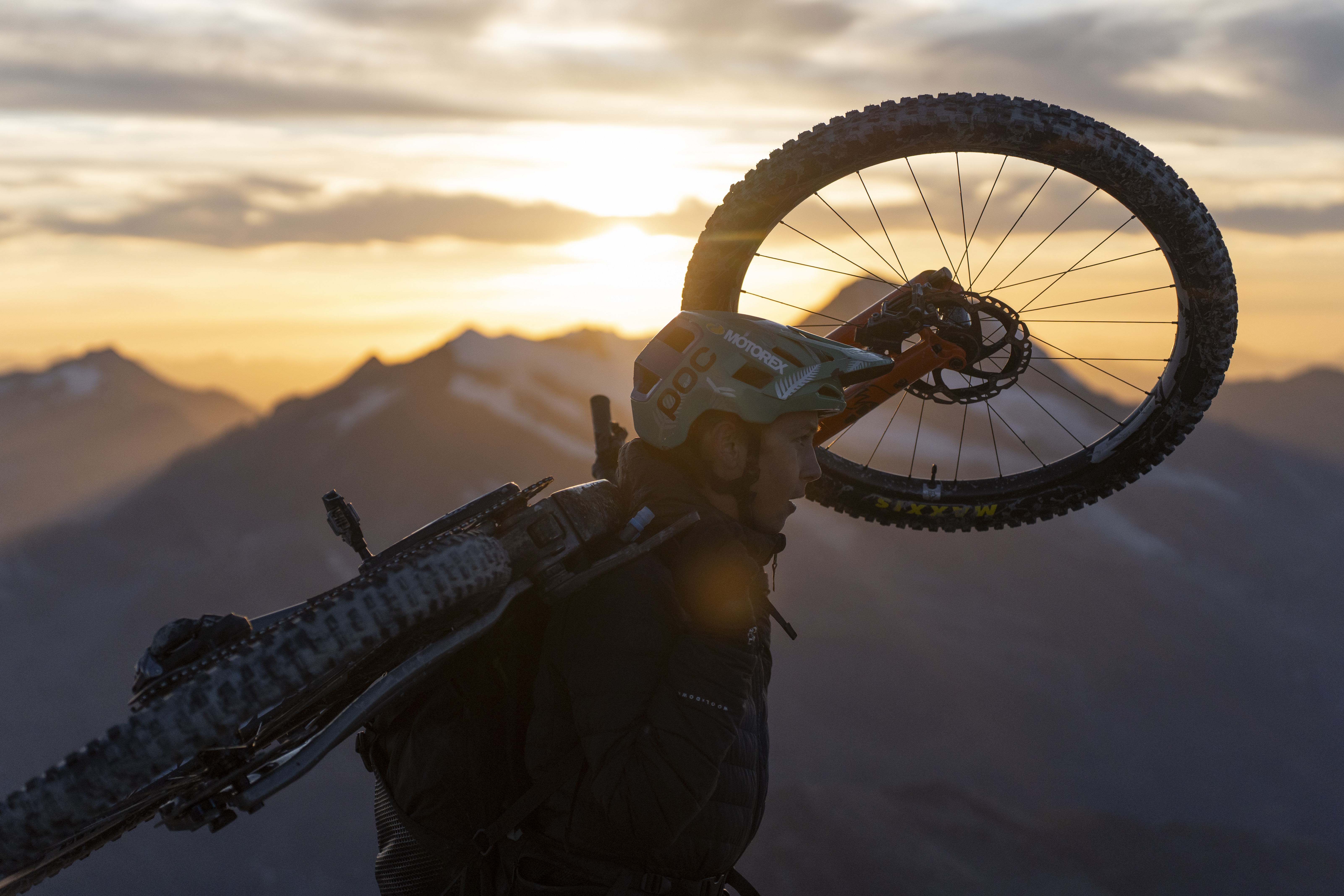 Matthew Fairbrother carries his bike equipped with Ergon components (saddle and grips) on his back as the sun rises over the mountain peaks.
