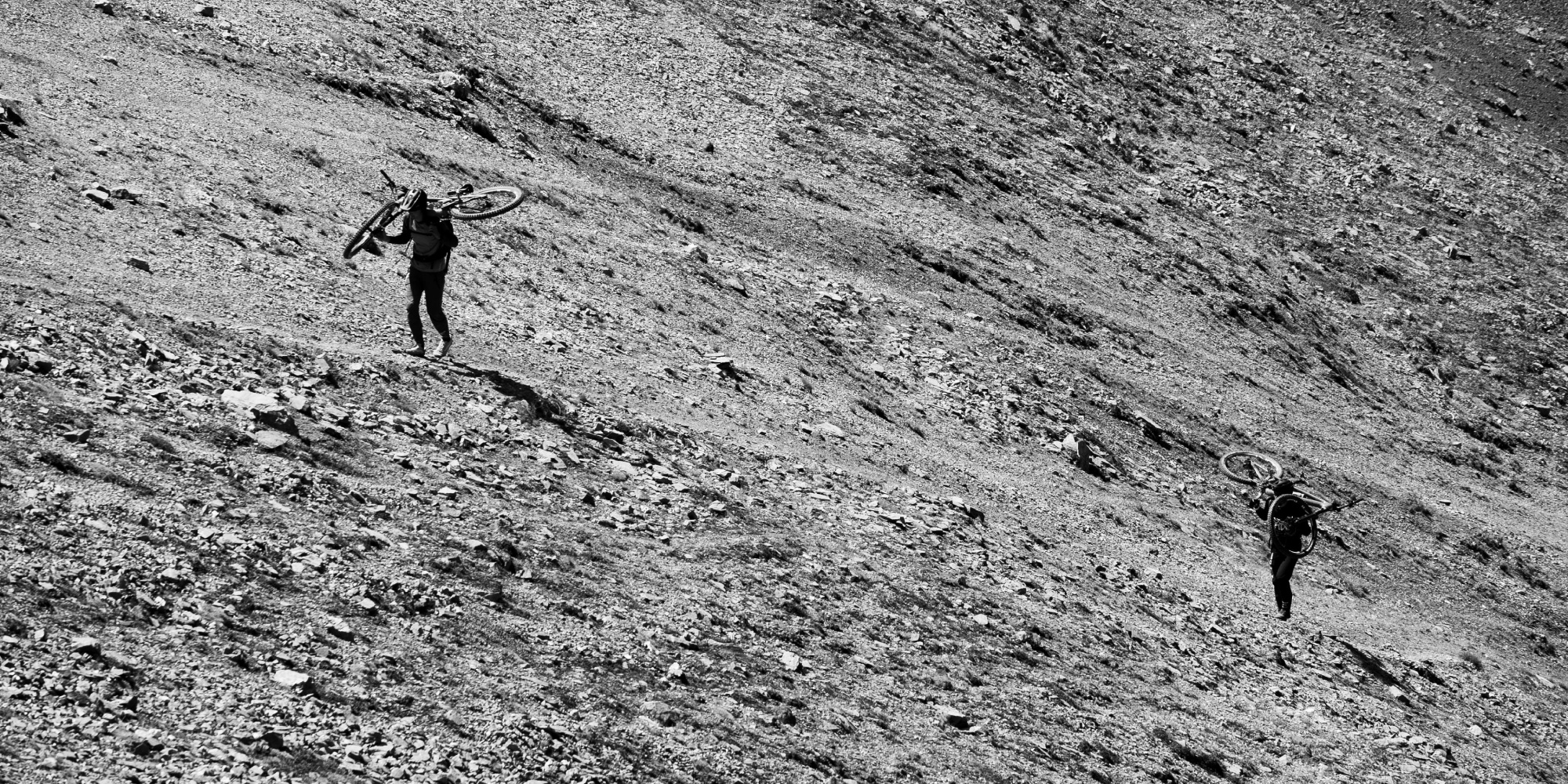 Two people carry their bikes up a steep incline.