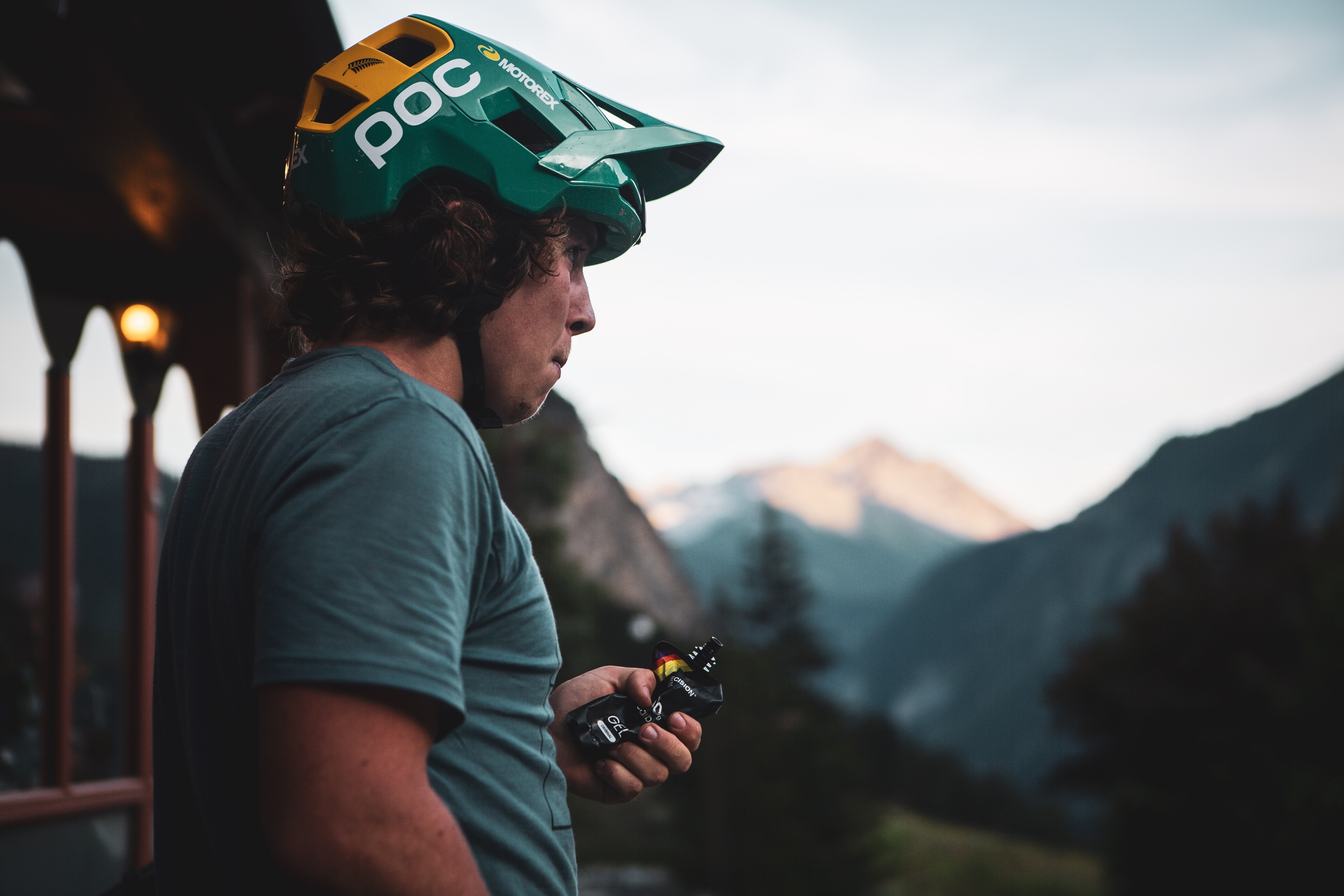 Matthew Fairbrother mit Helm hält Power Gel, Berge im Hintergrund, ruhige Umgebung.