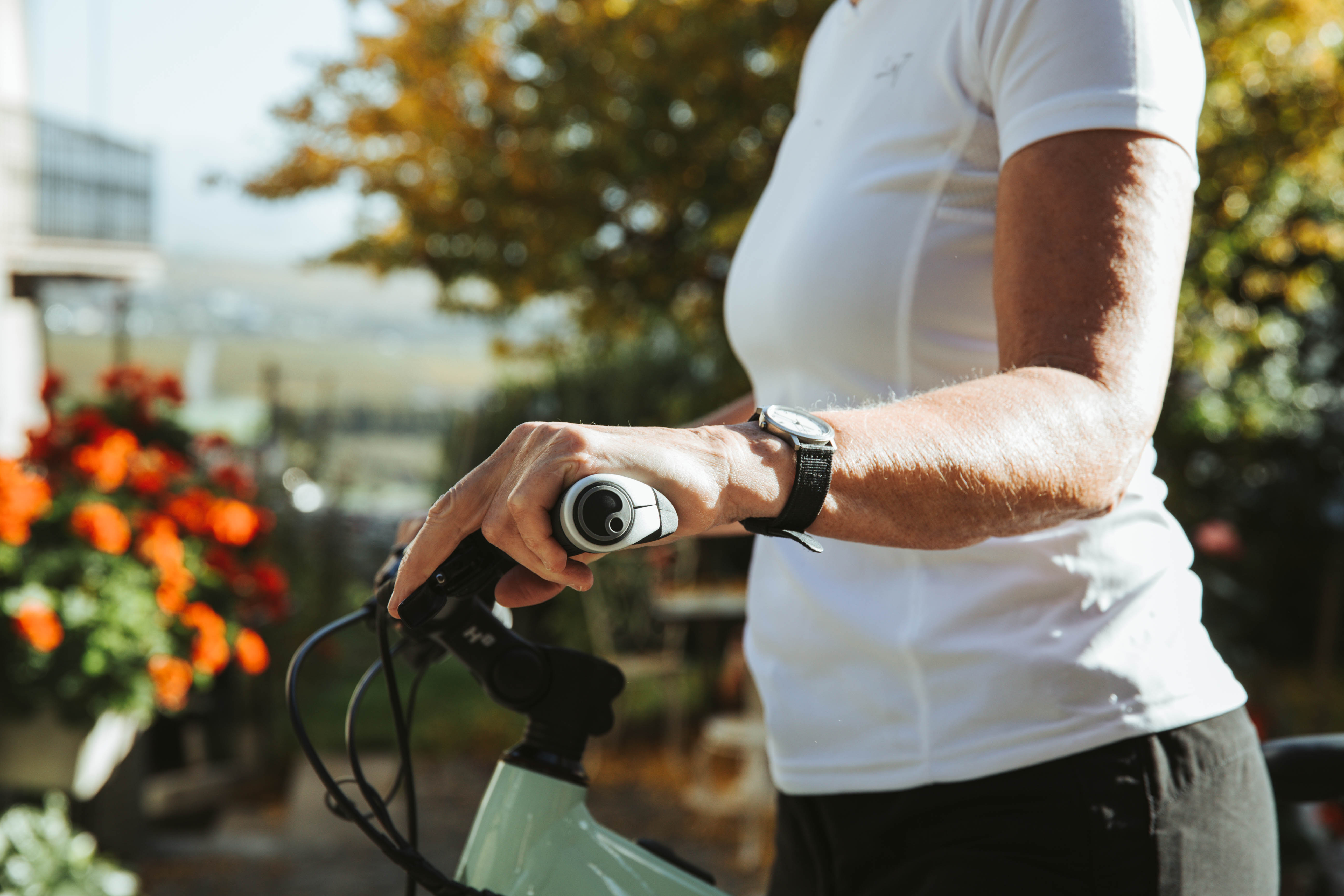 Eine Person hält den ergonomischen Fahrradgriff GP1 Evo von Ergon, während sie ein Fahrrad lenkt. Im Hintergrund blühen orangefarbene Blumen.