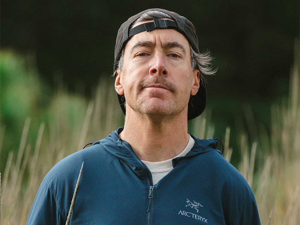 A portrait of Nate Hills wearing a blue rain jacket and a backwards cap.