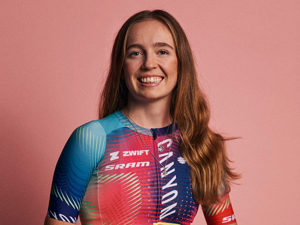 Portrait of Antonia Niedermaier who is smiling and wearing her team jersey while standing in front of a pink background