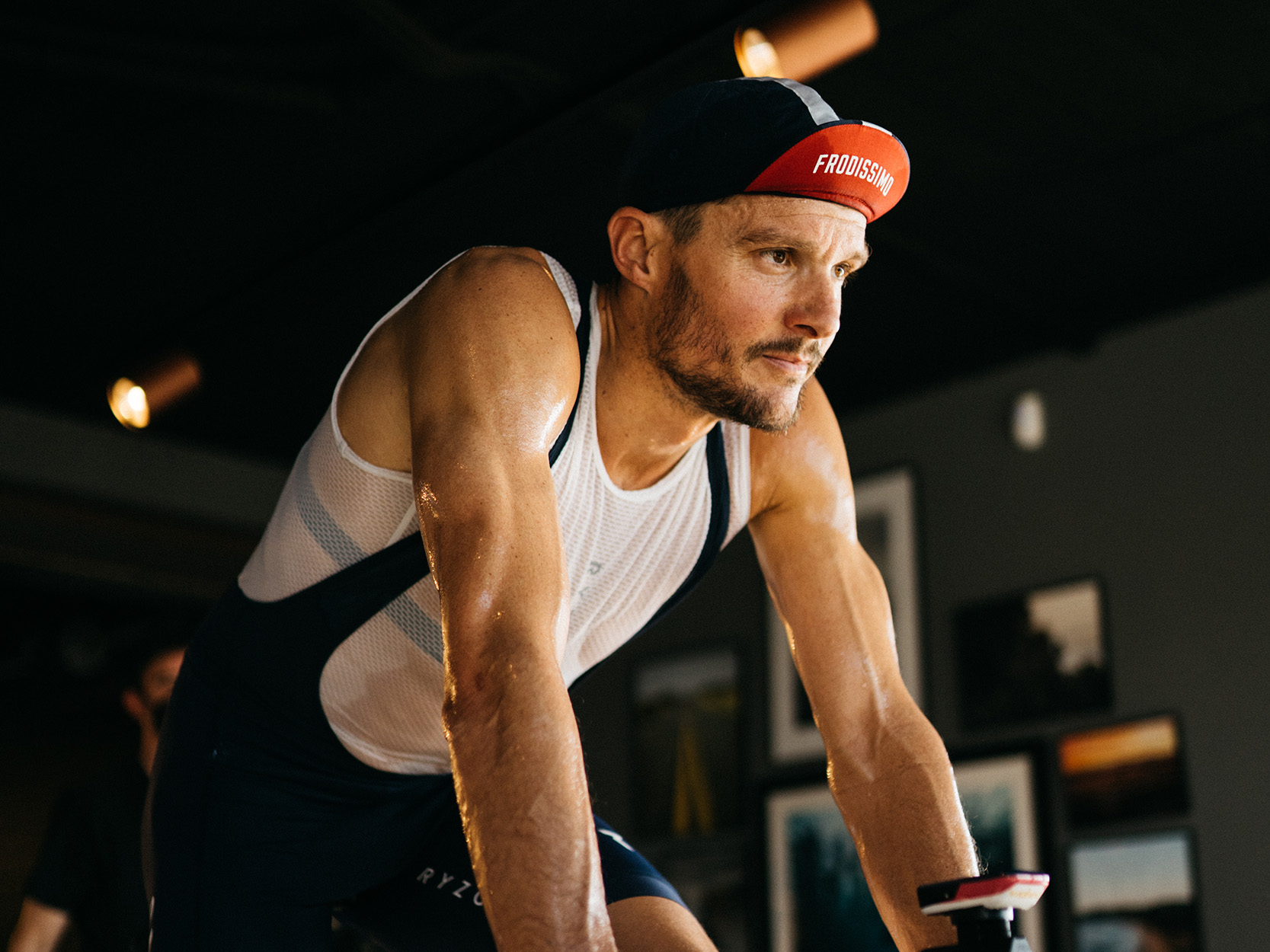 Jan Frodeno during indoor training, looking focused and wearing a printed cycling cap that says “Frodissimo”.