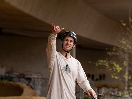 Portrait of Sam Pilgrim grinning at the camera and making the “hang loose” sign. 