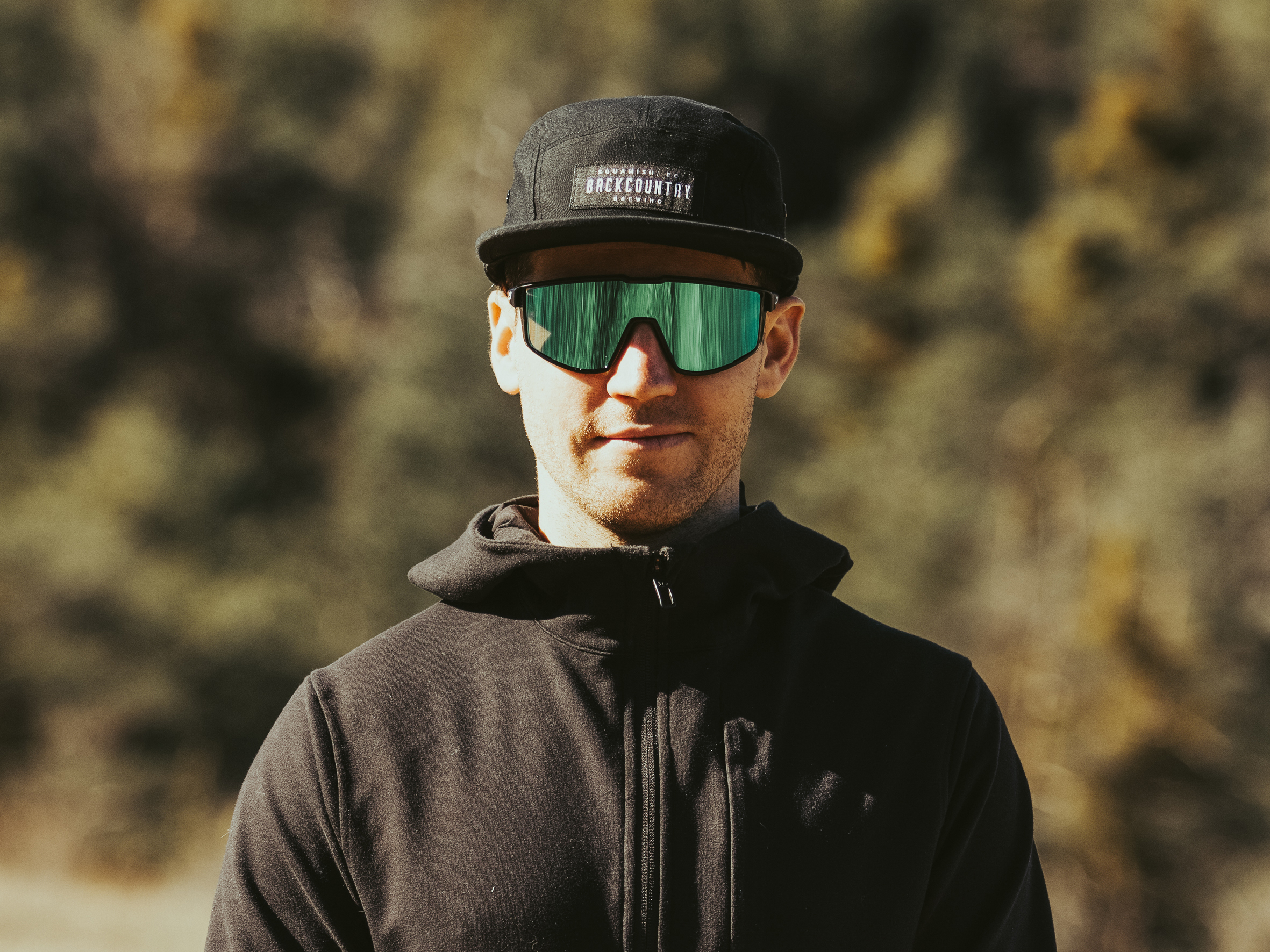 Portrait of Rémy Métailler wearing a black cap, jacket, and mirrored sunglasses. 
