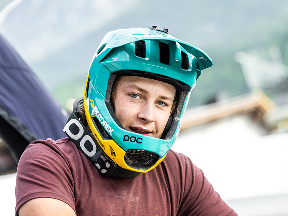 Porträt von Matthew Fairbrother mit rot-braunen T-Shirt und gelb-türkisen Fullface Helm.