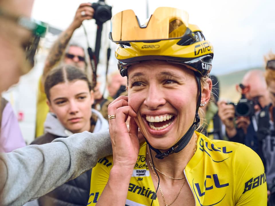 Kasia Niewiadoma appears euphoric as she is surrounded by a crowd of people and wears yellow cycling gear. 