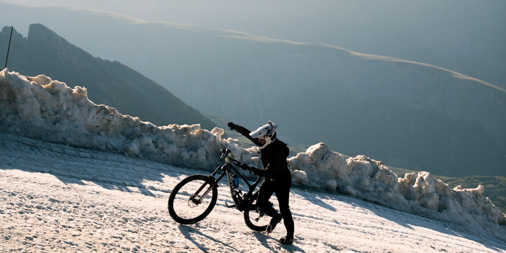 Mael schiebt sein Rad einen steilen Anstieg hoch. Im Hintergrund ist das Tal und weitere Berge zu sehen.