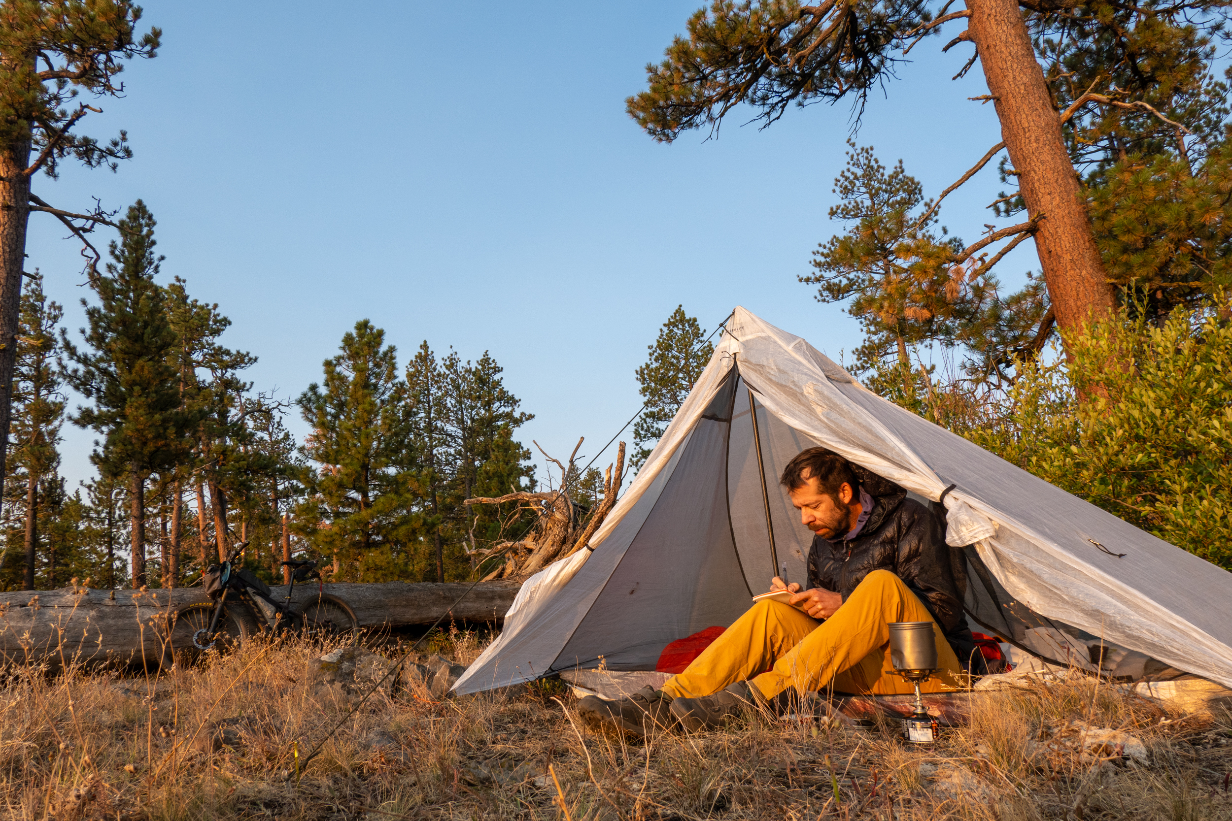 Ein Bikepacker entspannt in einem leichten Trekkingzelt während seines Long-Distance-Bikepacking-Abenteuers in Amerika. Das Bild zeigt die selbstversorgte Seite des Bikepacking auf dem Orogenesis Trail – mehrtägige Etappen, minimalistisches Equipment und Übernachtungen in der Natur entlang einer der anspruchsvollsten Ultra-Endurance-Mountainbike-Routen Nordamerikas.