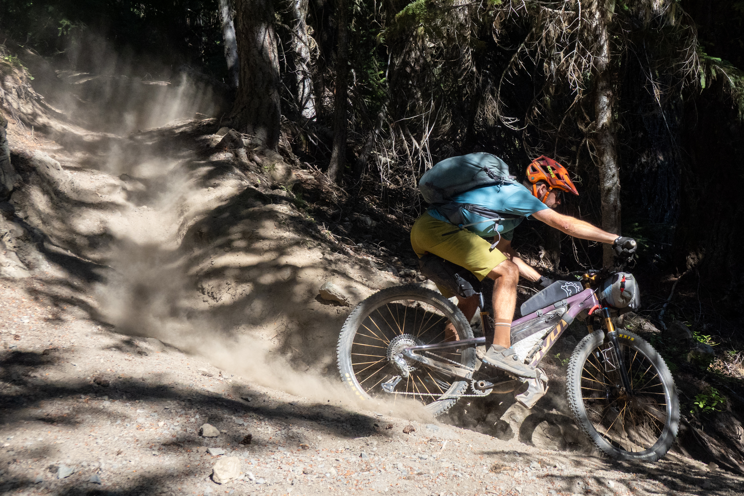 Ein Bikepacker fährt mit beladenem Mountainbike über einen staubigen Singletrail im Wald während seines Long-Distance-Bikepacking-Abenteuers in Amerika. Das Bild zeigt die körperliche Herausforderung und Dynamik des Orogenesis Trail – eine der anspruchsvollsten Ultra-Endurance-Mountainbike-Routen von der US-kanadischen Grenze bis nach Baja California.