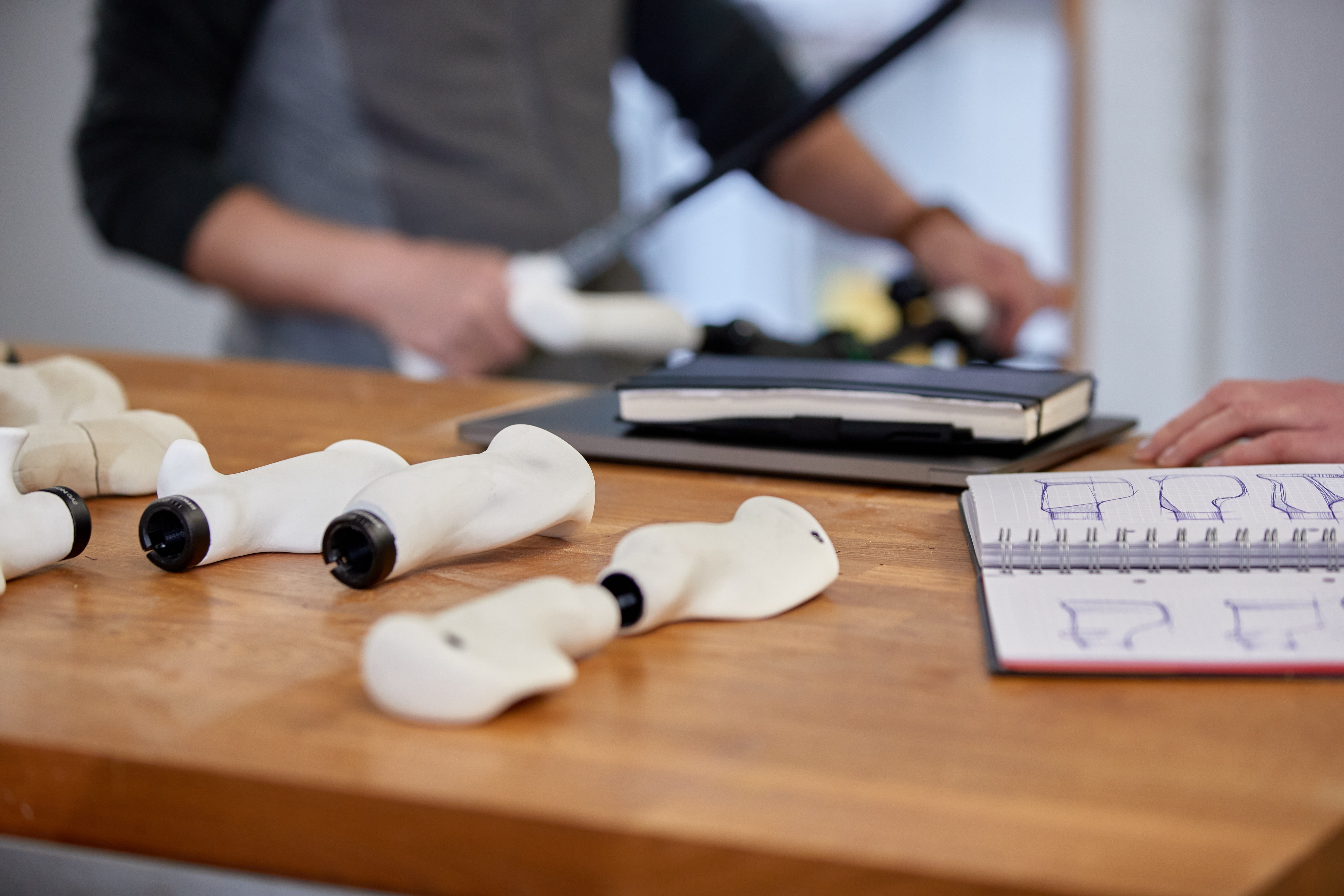 Modell-Fahrradgriffe und Skizzenbuch auf einem Tisch, im Hintergrund montierte Modell-Fahrradgriffe von Ergon. 