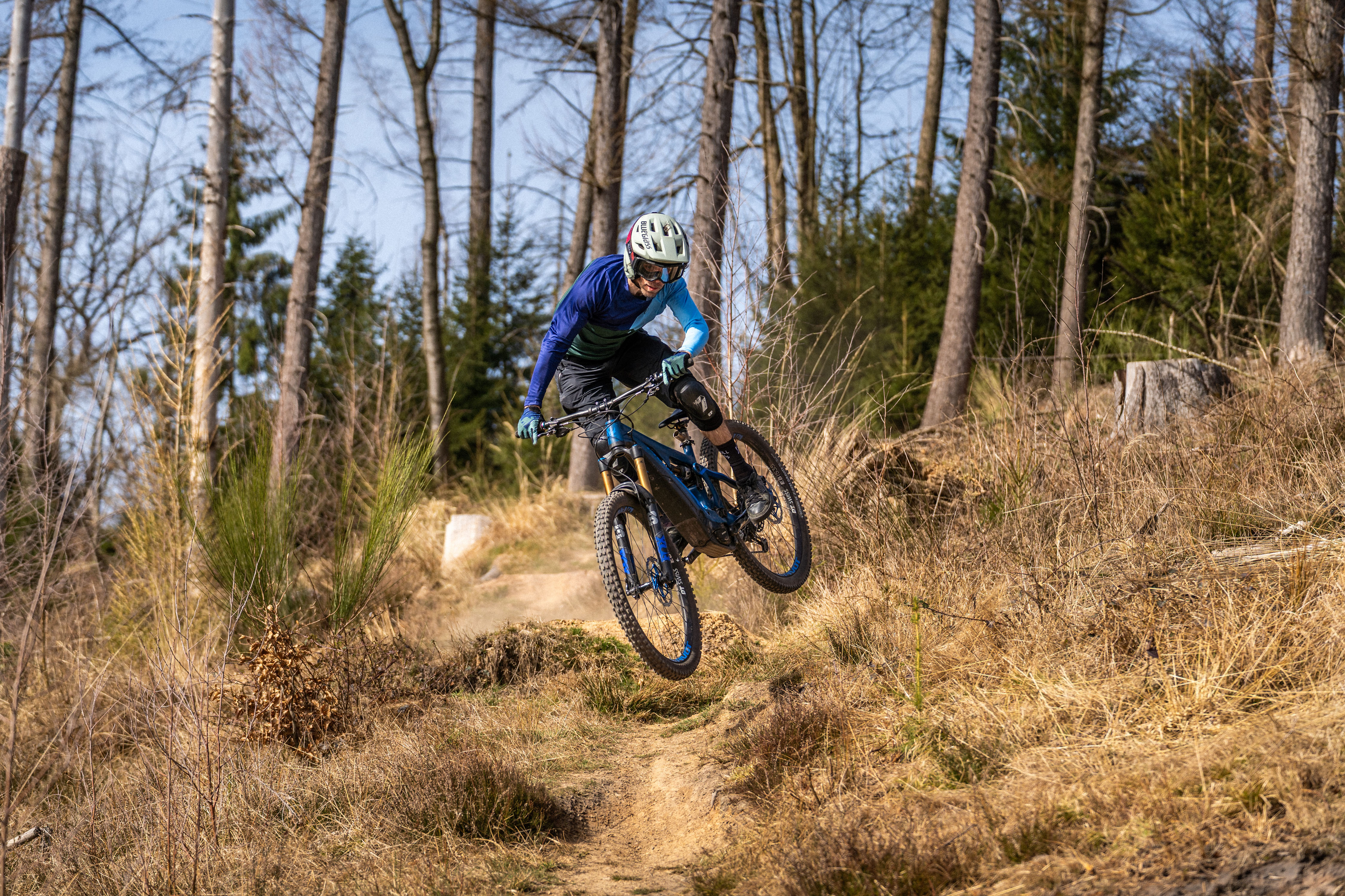 E-Mountainbike-Fahrer beim Sprung auf einem anspruchsvollen Waldtrail, dynamische Offroad-Performance