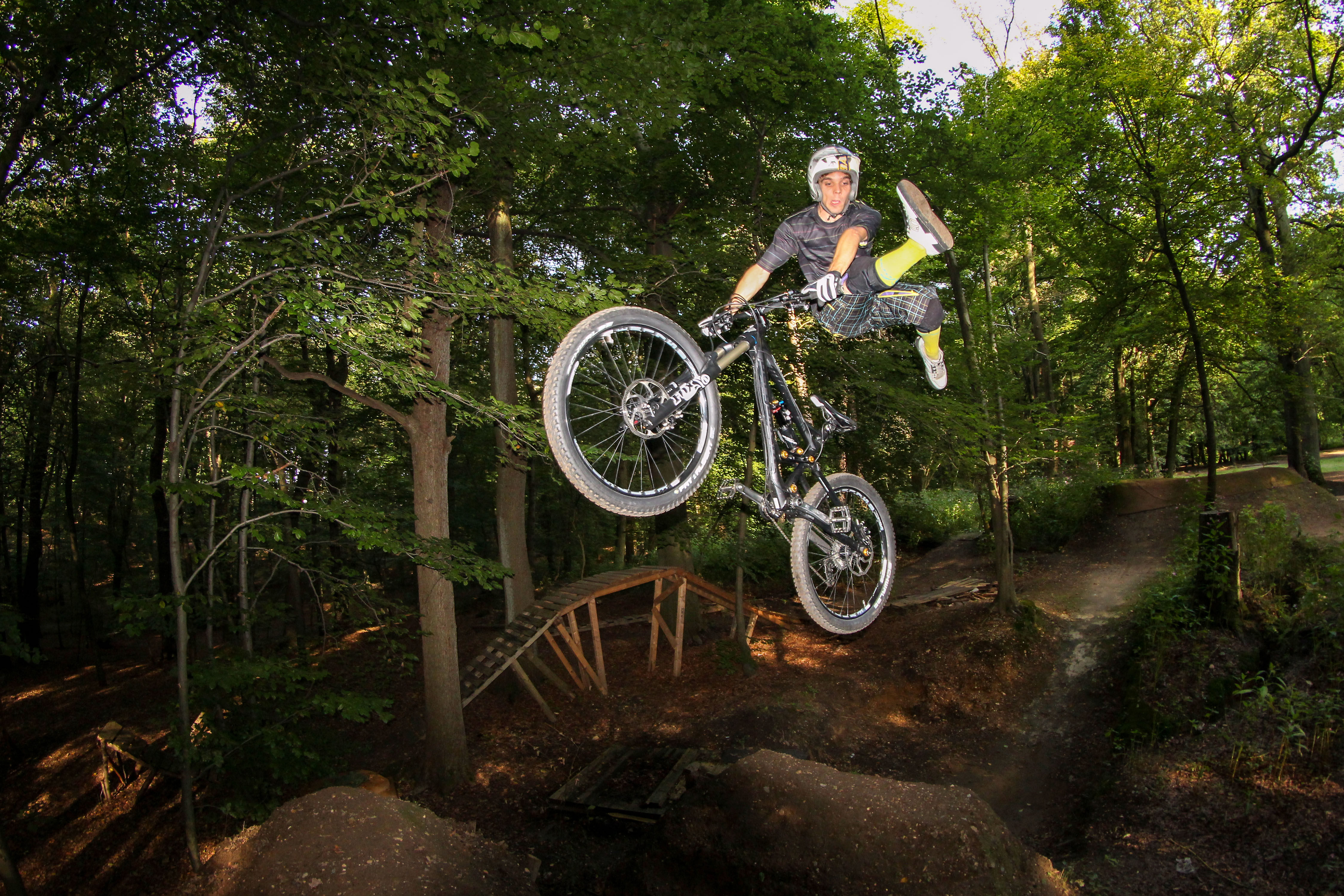 Mountainbiker zeigt einen Oldschool-Freeride-Trick bei einem Sprung im Bikepark Bendorf. Dynamische MTB-Action in bewaldeter Umgebung mit viel Airtime und klassischem Gravity-Style.