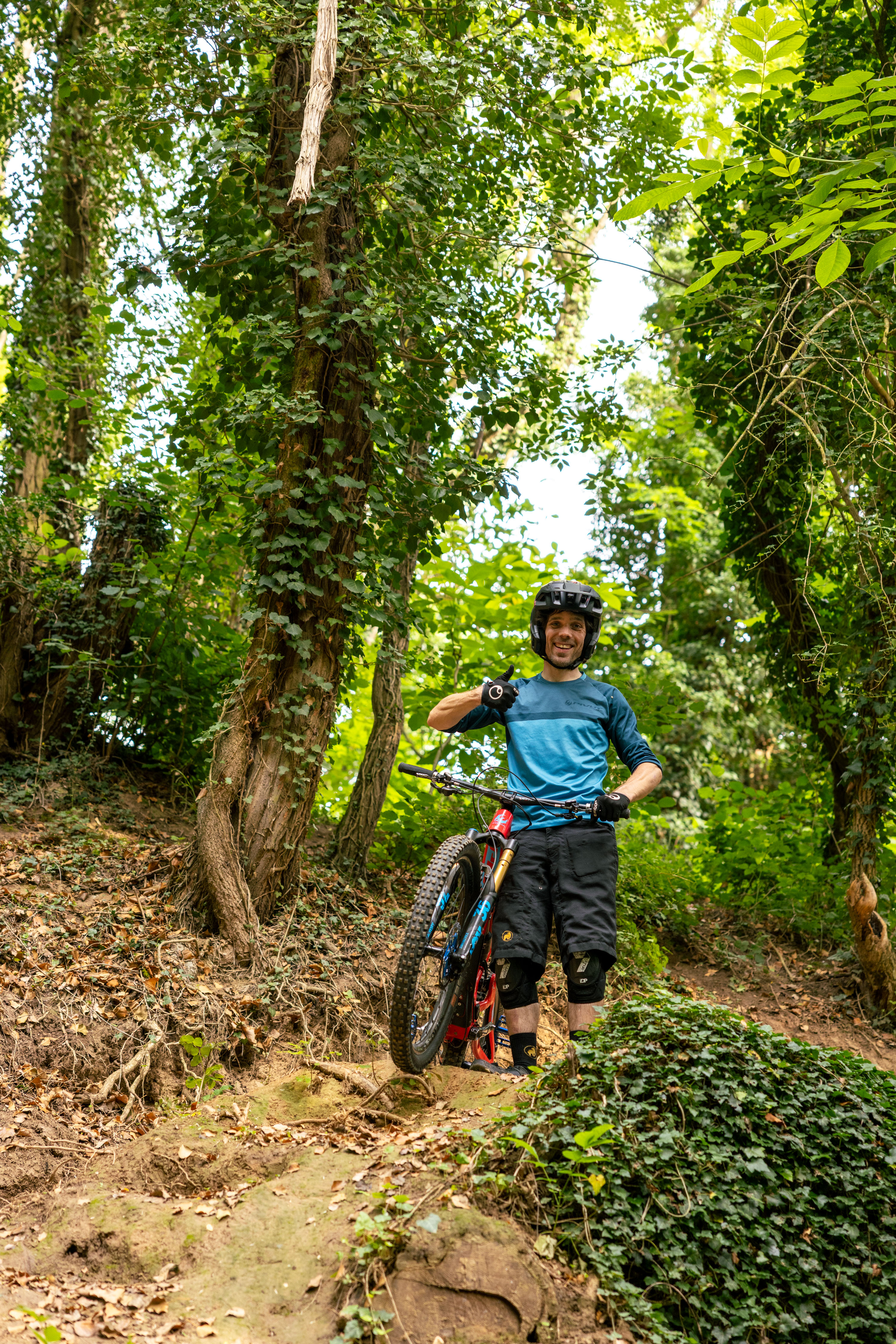 Mountainbiker Sascha “Bam Hill” Bamberg standing with his bike on a forest freeride trail in Bikepark Bendorf.
