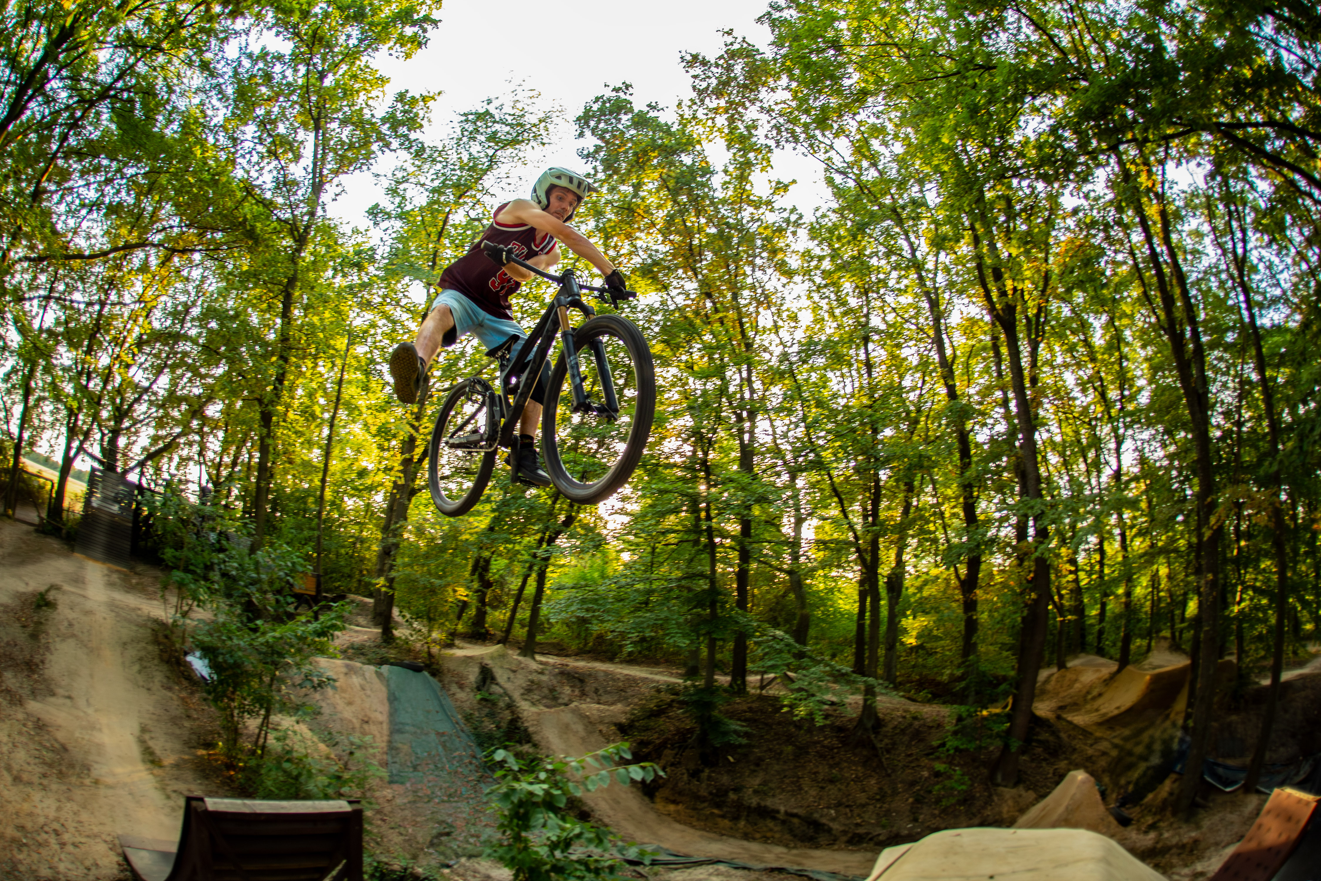 Mountainbiker zeigt einen stylischen Dirtjump-Sprung mit viel Airtime auf einem Trail im Wald von Compton. Dynamische MTB-Action in natürlicher Umgebung mit flachem Whip und klassischem Freeride-Style.