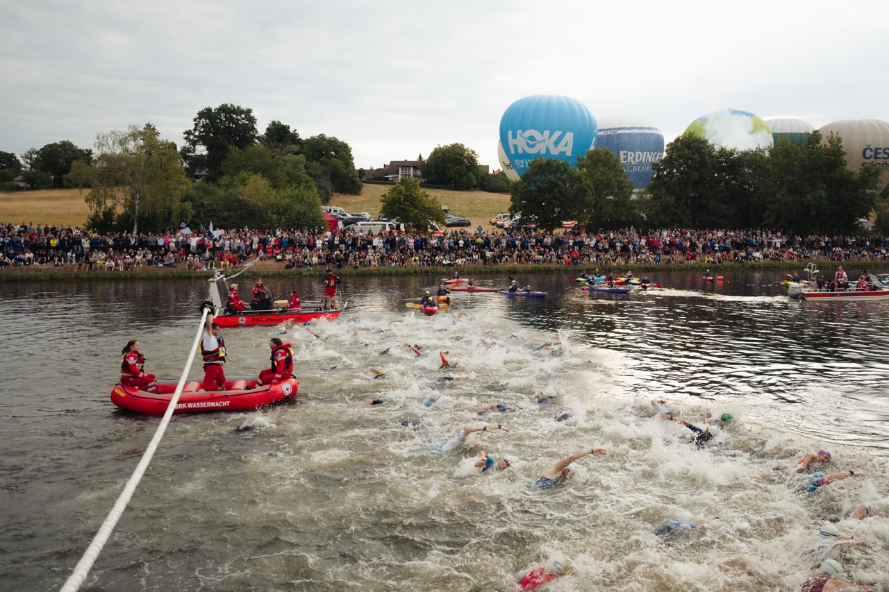 Viele Menschen schwimmen beim Triathlon in Roth einen Fluss entlang