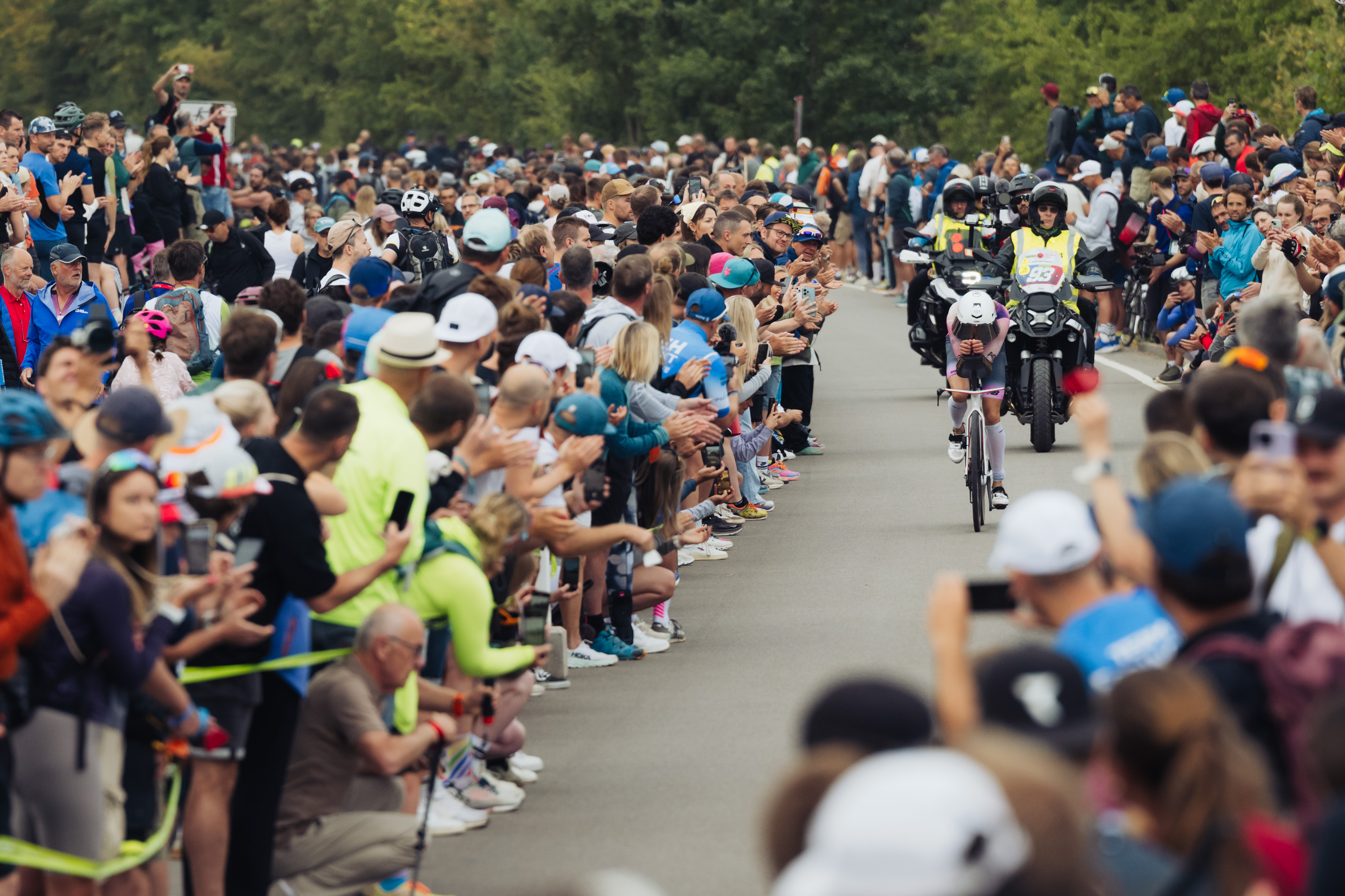 Laura Phillip auf dem Fahrrad beim Triathlon. Links und rechts neben der Strecke stehen zahlreiche Zuschauer.