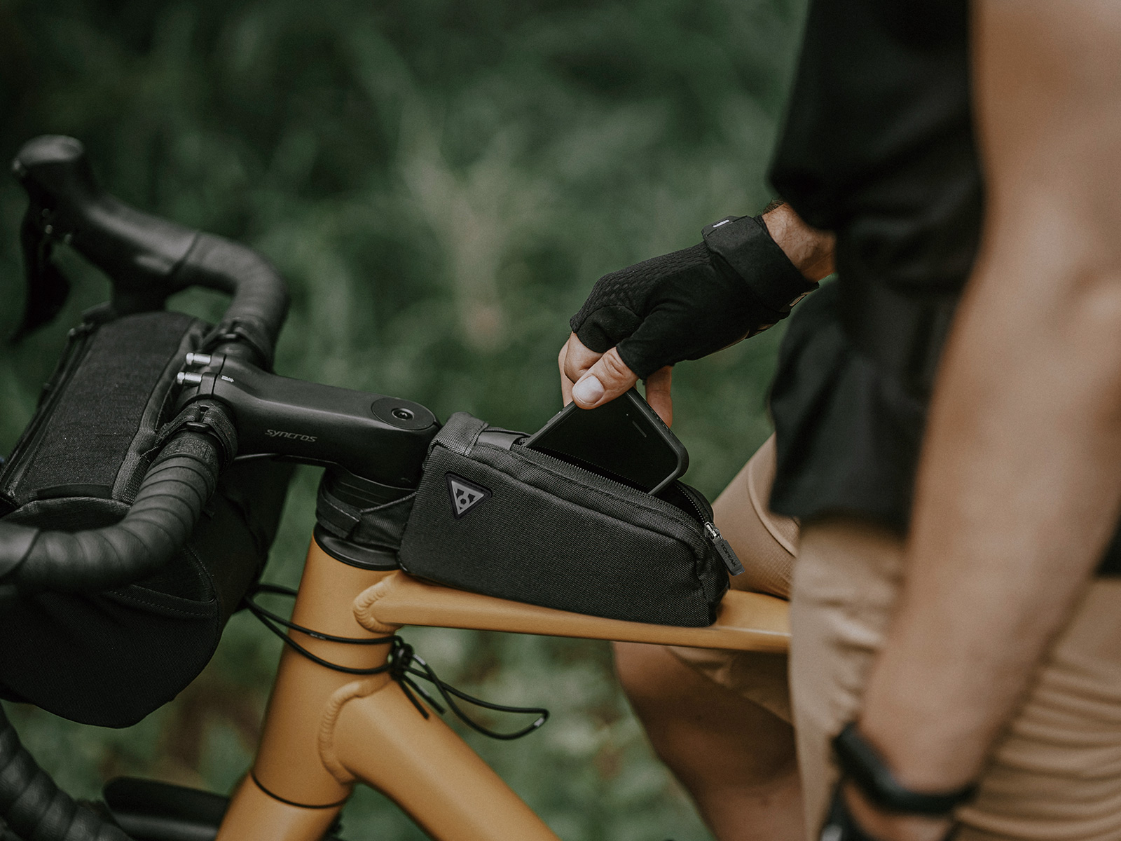 Oberrohrtasche am Gravelbike. Der Fahrer verstaut sein Smartphone in der Tasche.