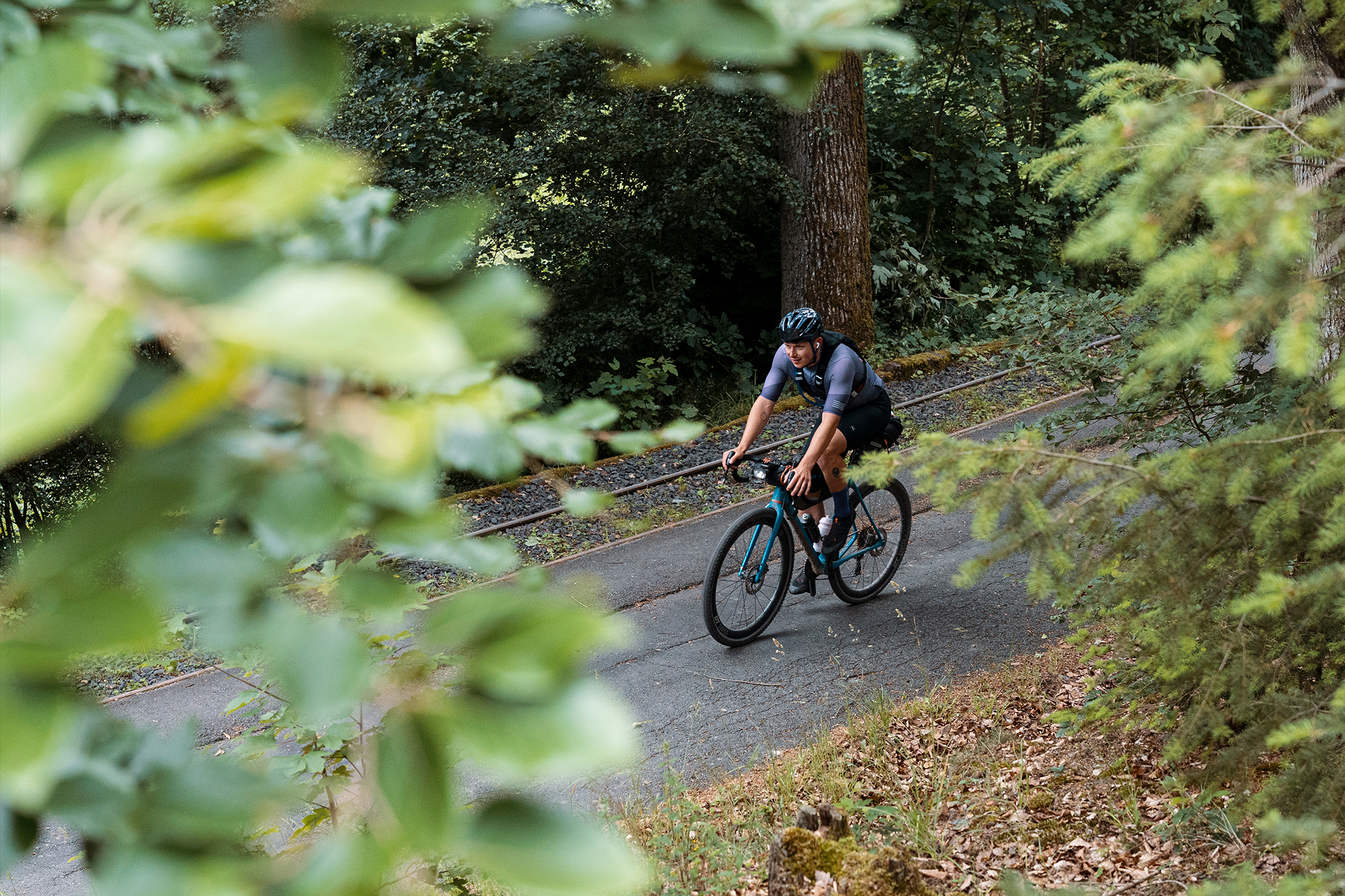 Cyclist on a narrow forest trail, framed by out-of-focus green leaves in the foreground
Photographer Jakab Rokob
