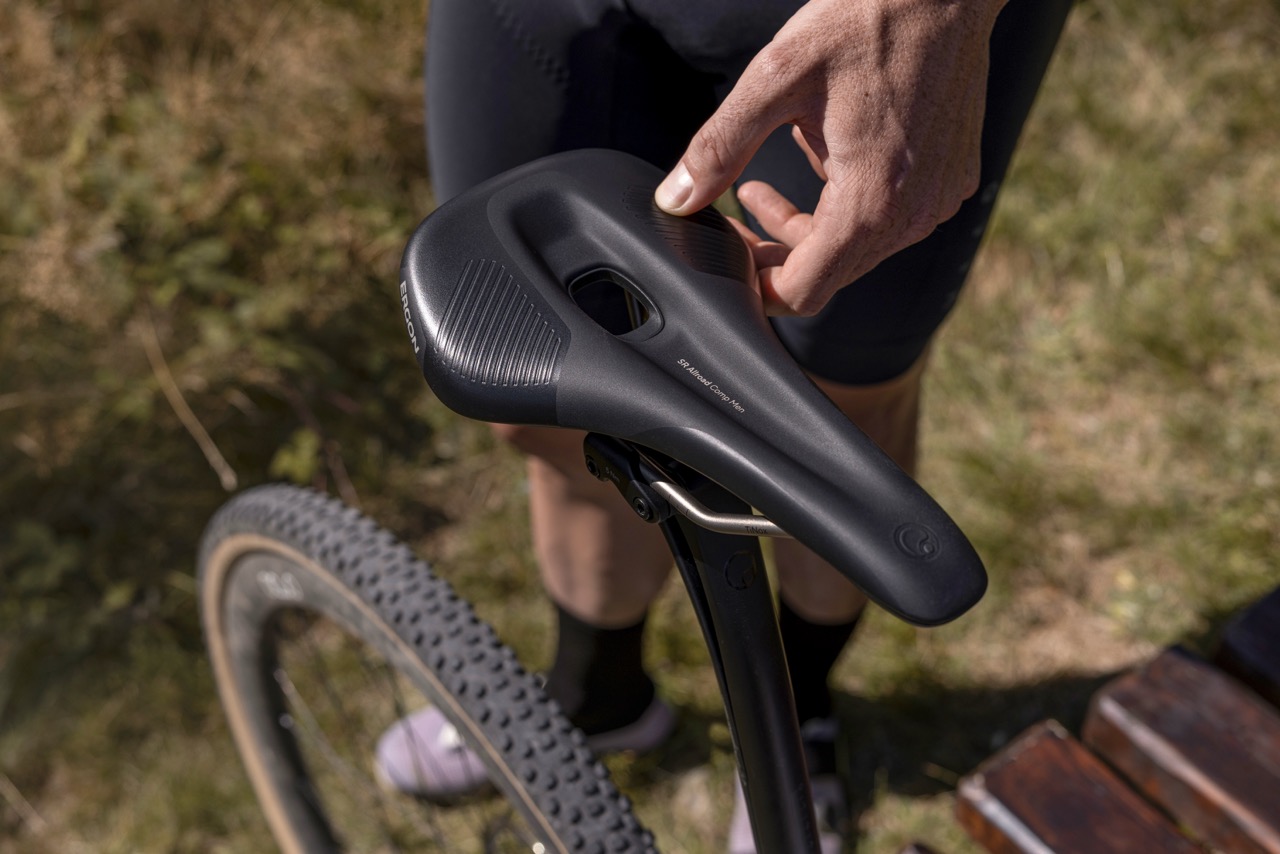 A hand adjusts a bike component near the saddle area in a forest setting