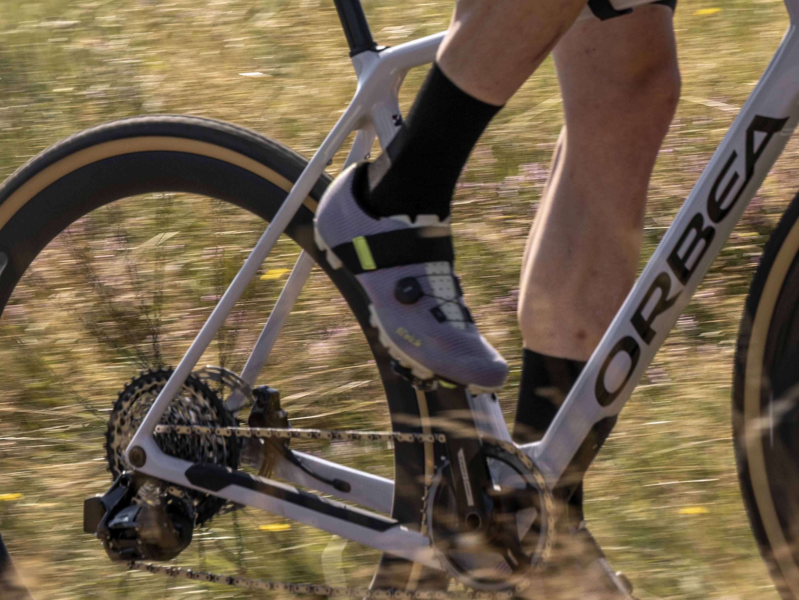 Motion-blurred close-up of an gravel bike with the rider's leg visible in the background