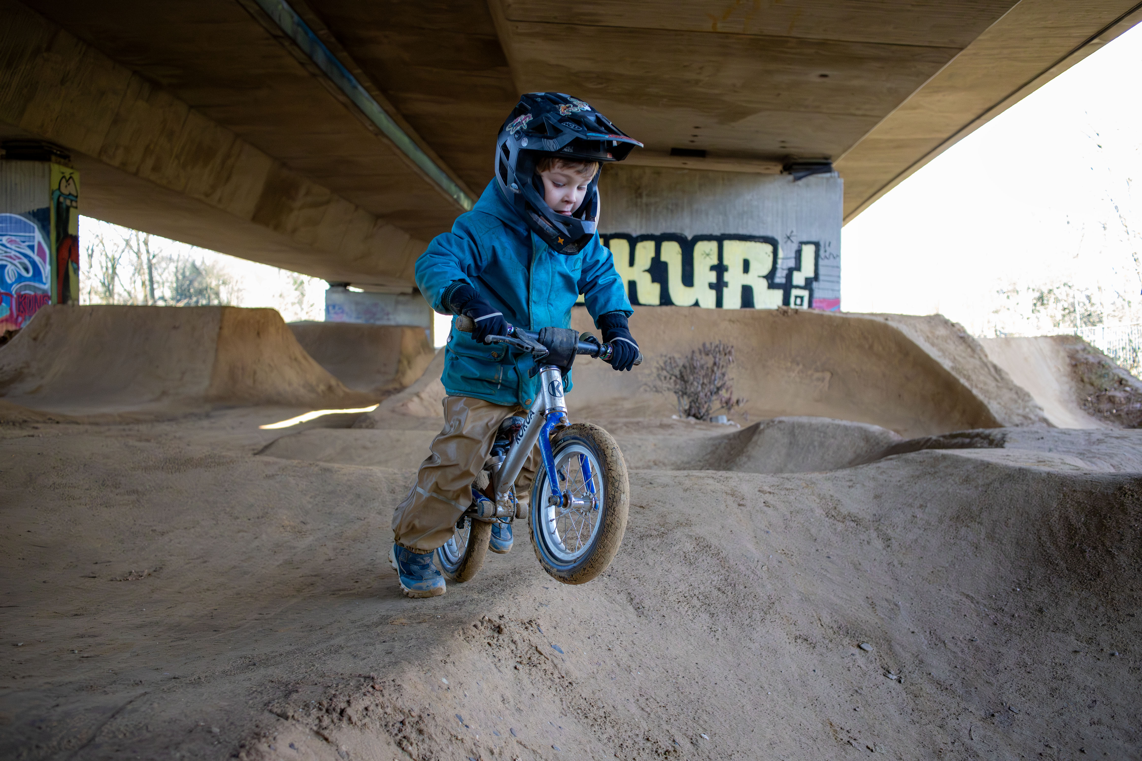 Ein kleiner Junge fährt mit seinem Laufrad über einen Pumptrack