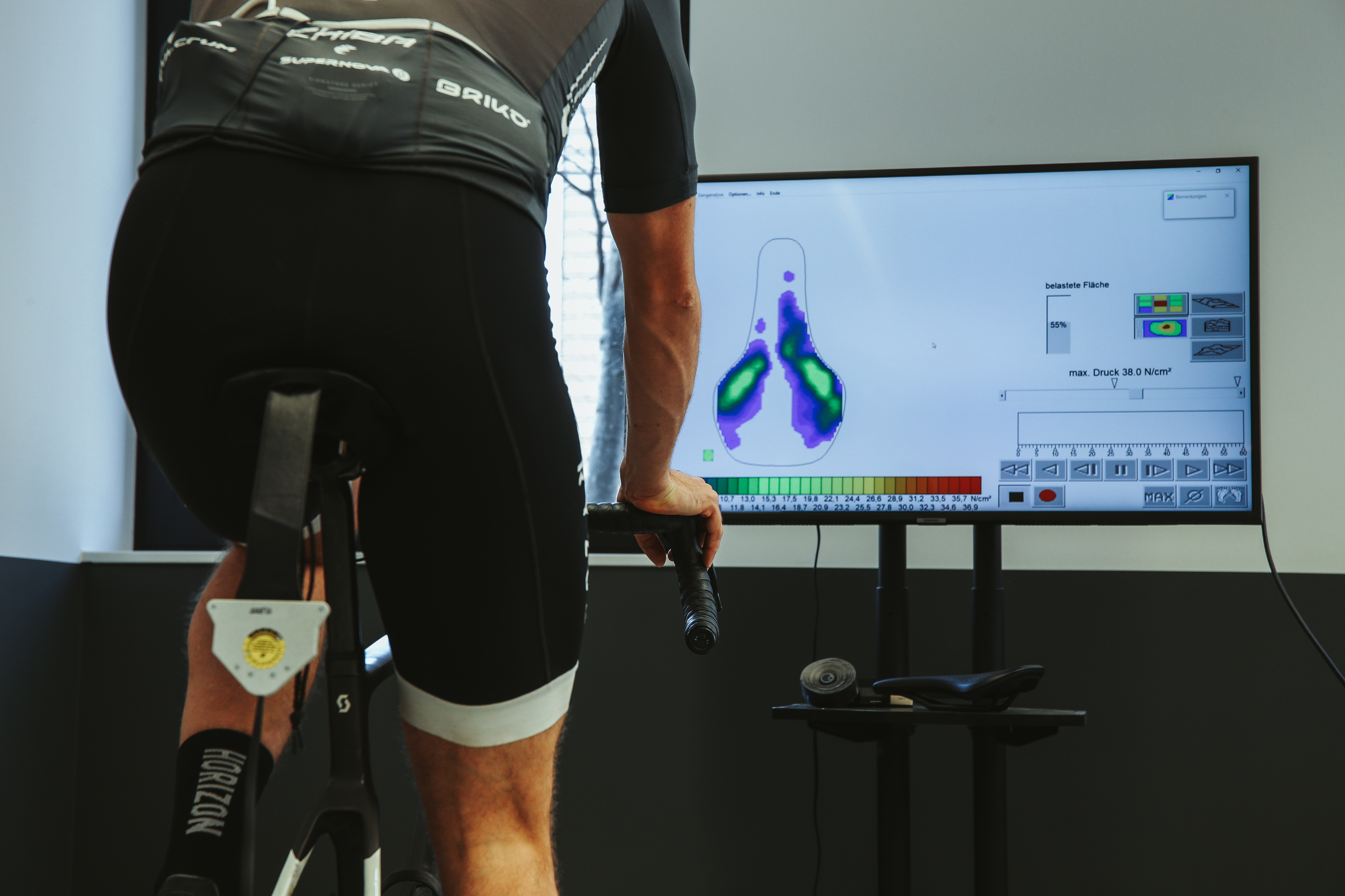 Jonas Deichmann während einer Sitzpositionsanalyse auf seinem Rennrad. Auf dem Bildschirm im Hintergrund wird die Druckverteilung auf dem Sattel angezeigt