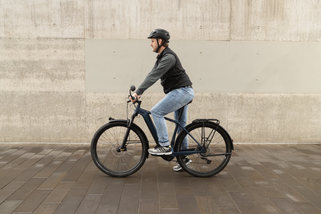 Mann steht mit Fahrrad vor einer Mauer. Aufnahme von der Seite.