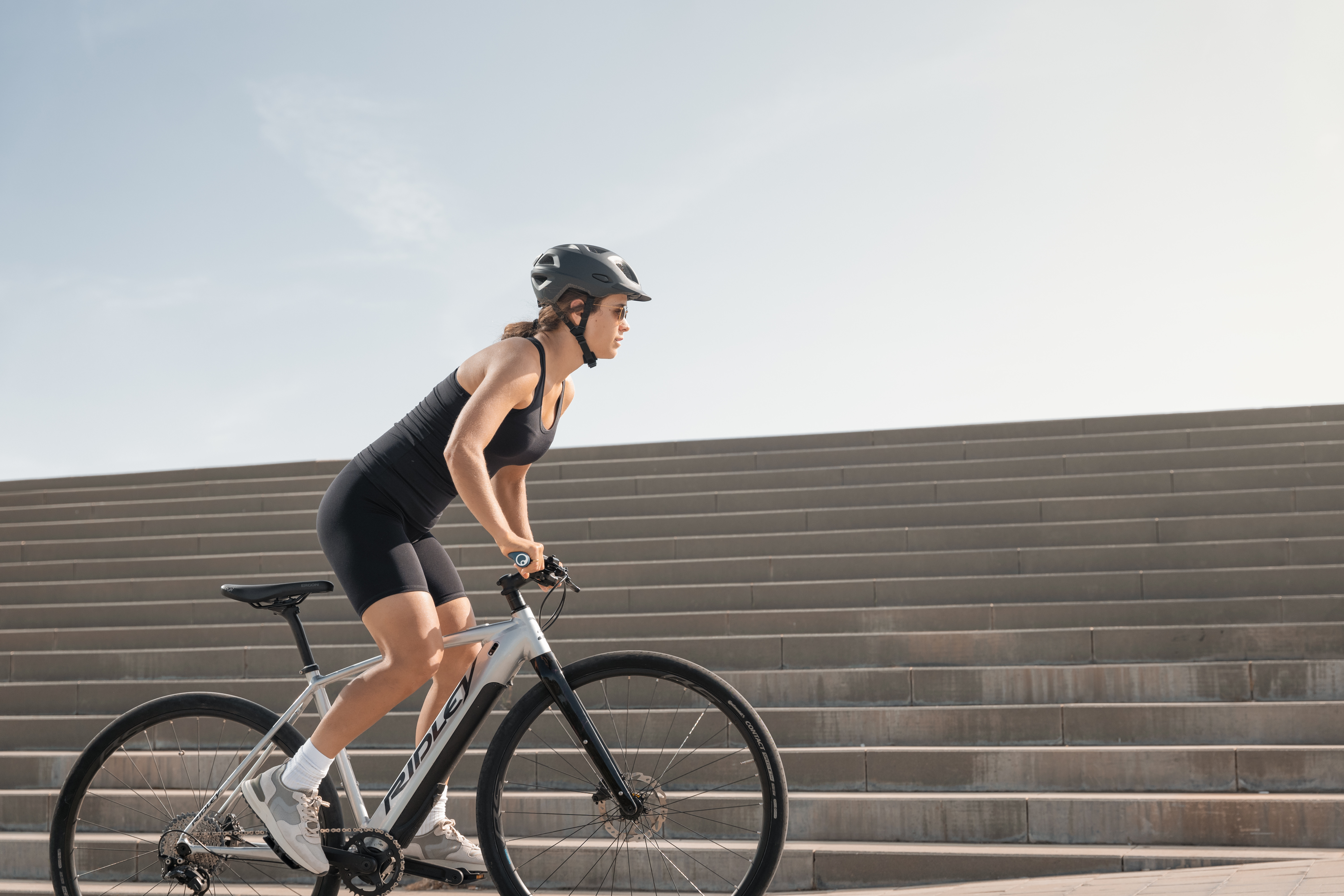 Frau auf Fitnessrad, steht leicht gebeugt auf den Pedalen