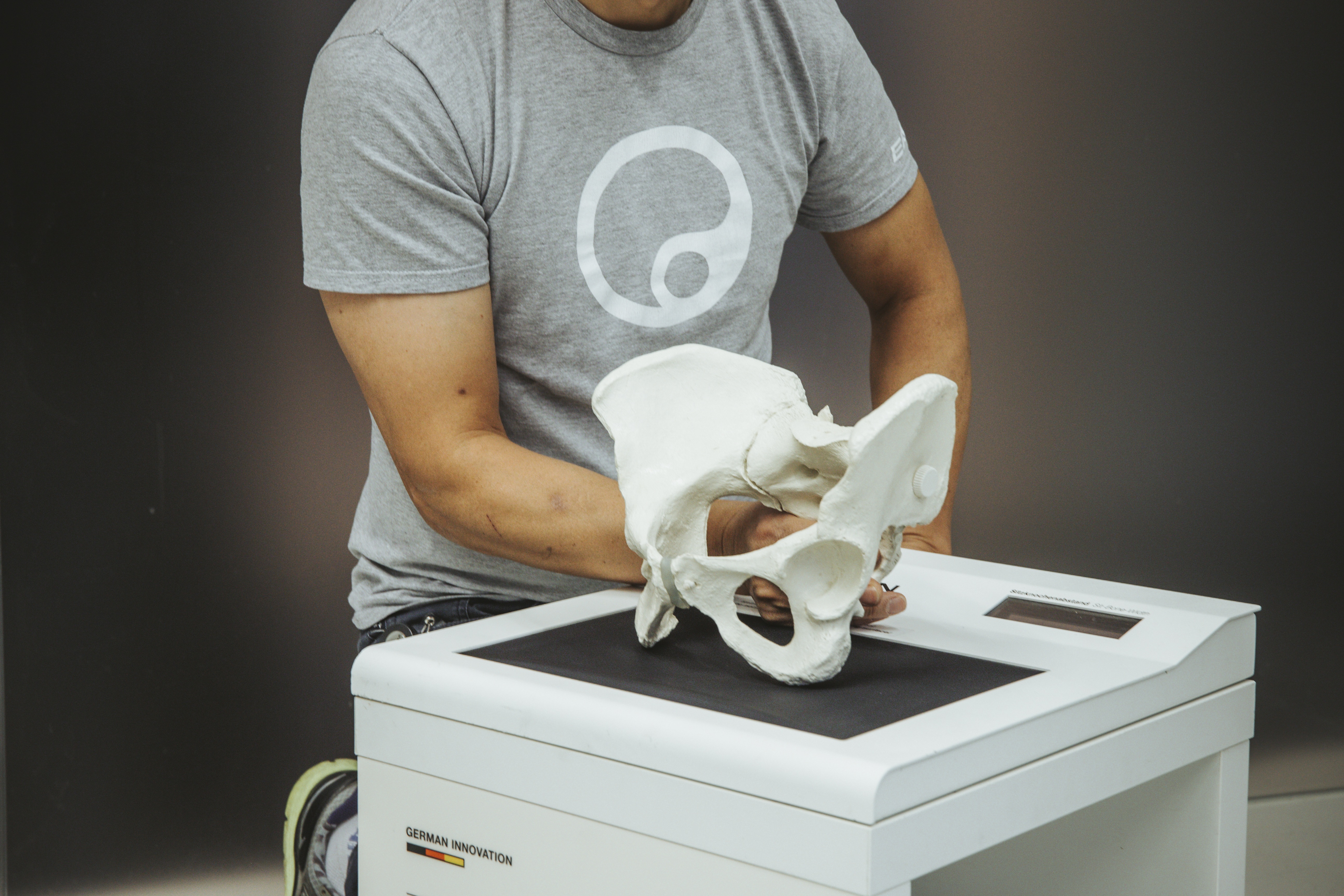 Eine Person hält ein Modell eines menschlichen Beckens und zeigt, wie man den Sitzknochenabstand mit "Ergon TS1" misst.