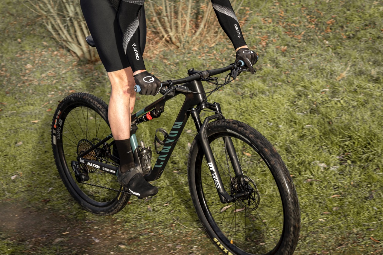 MTB Cleats Mann fährt mit MTB über eine Wiese. Er trägt Schuhe für Klickpedale.