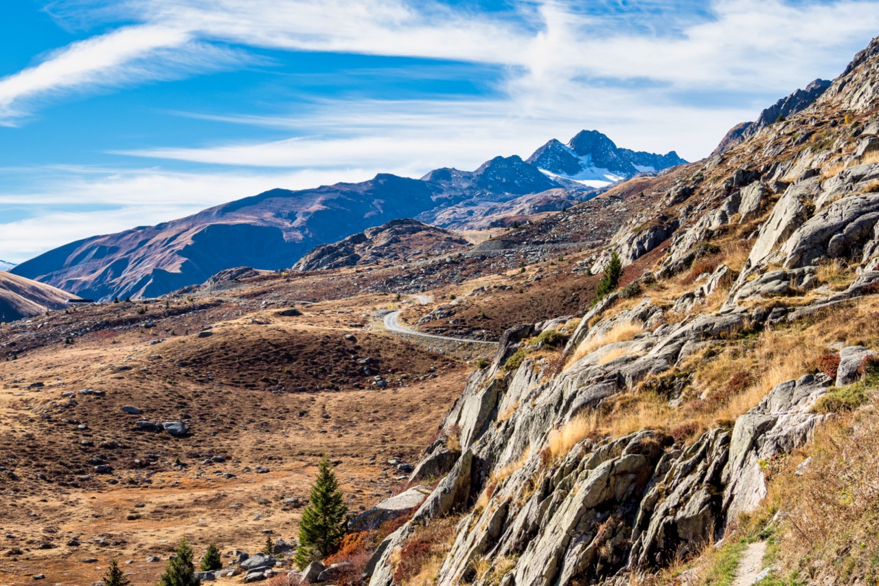 Radfahrer auf dem Col de la Croix de Fer mit Blick auf schneebedeckte Gipfel und Almwiesen.