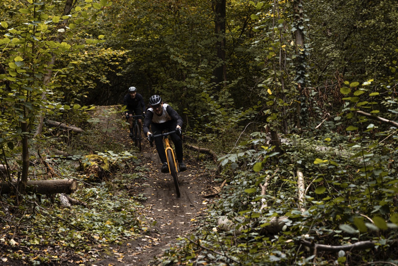 Two men riding their gravel bikes through a forest