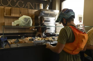 Matthew Fairbrother steht in einer Bäckerei/Pizzeria, umgeben von Auslagen, und lädt während seiner Tour mit Ergon-Sattel und Griffen Energie nach.