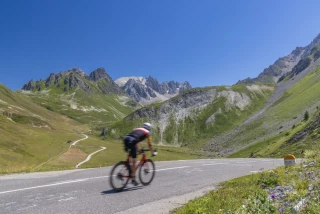 Col du Galibier Cyclist on Col du Galibier with views of snow-capped peaks and alpine meadows.