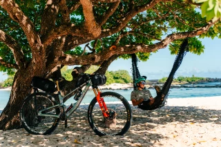 Fairbrother-Samoa-Hammock Matthew Fairbrother having a break on a hammock. His bike is leaned against a tree.