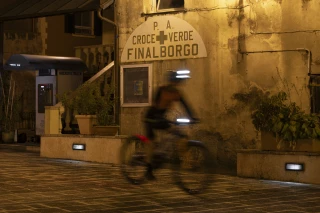 Vor einem beleuchteten Gebäude in Finale Borgo rauscht Matthew Fairbrother auf seinem Bike mit Ergon-Sattel und Griffen vorbei. Das warme Licht kontrastiert mit der nächtlichen Szene.