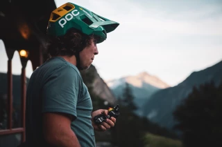 Ergon Cyclist Matthew Fairbrother Matthew Fairbrother with helmet holding Power Gel, mountains in the background, calm environment.