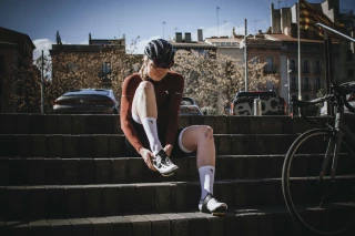 Warum werden meine Zehen beim Radfahren taub? – Ergon Lösungen Fahrradfahrerin zieht Radschuhe auf einer Treppe an.